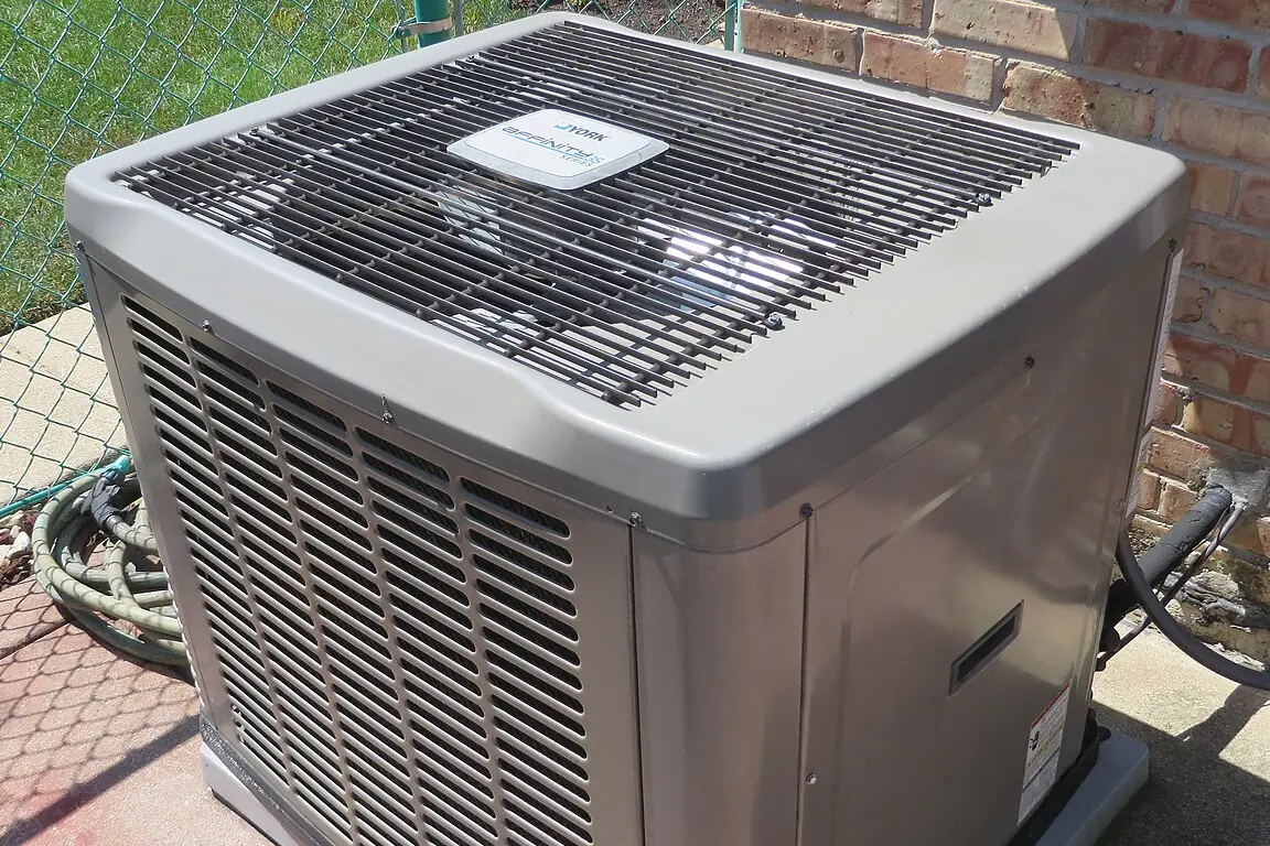 Central air conditioning condenser on a concrete pad beside a brick wall