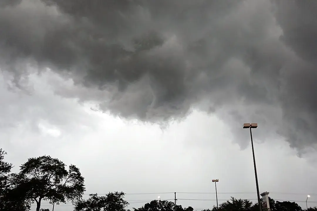 Dark thunderstorm clouds building over a parking lot and trees