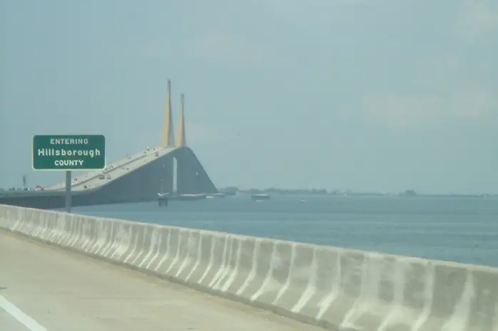 County line sign beside a highway on the approach to a tall cable-stayed bridge over the bay