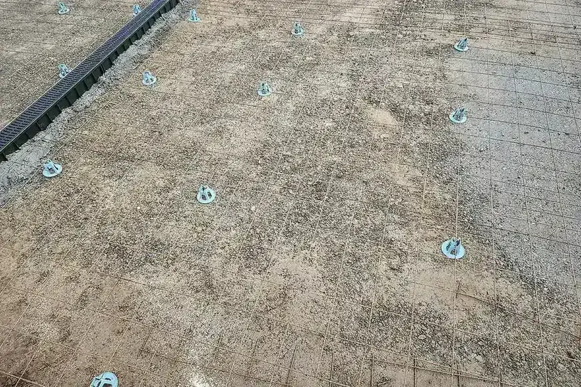 Steel mesh on plastic chairs over a prepared base with a channel drain at the edge