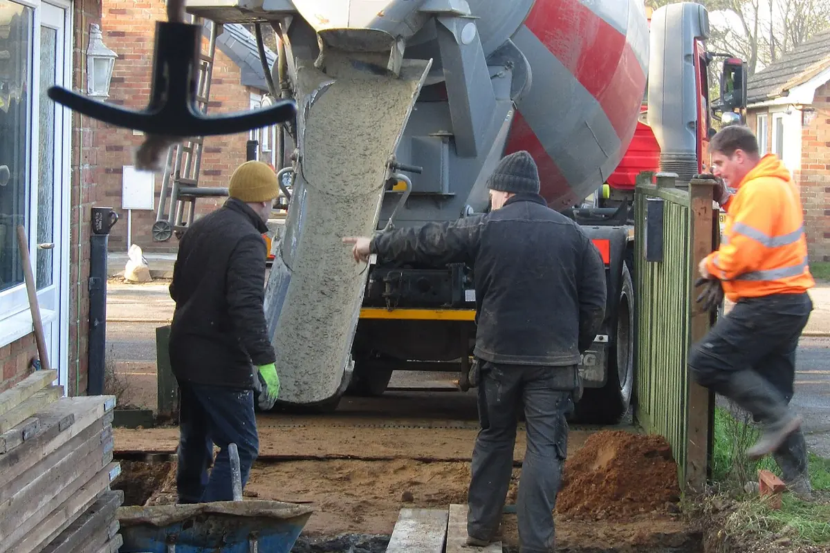 Mixer truck chute placing concrete into a footing trench beside a brick house