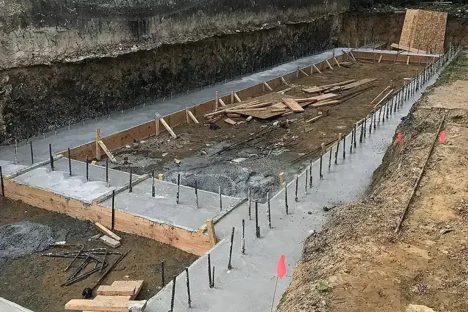 Excavated footing trench with wood forms and steel dowels beside an existing wall
