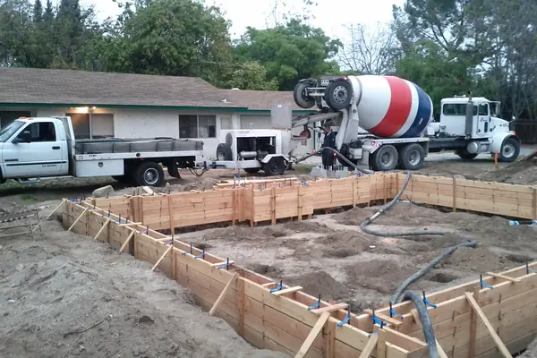 Mixer truck and pump hose at wood foundation forms beside a house