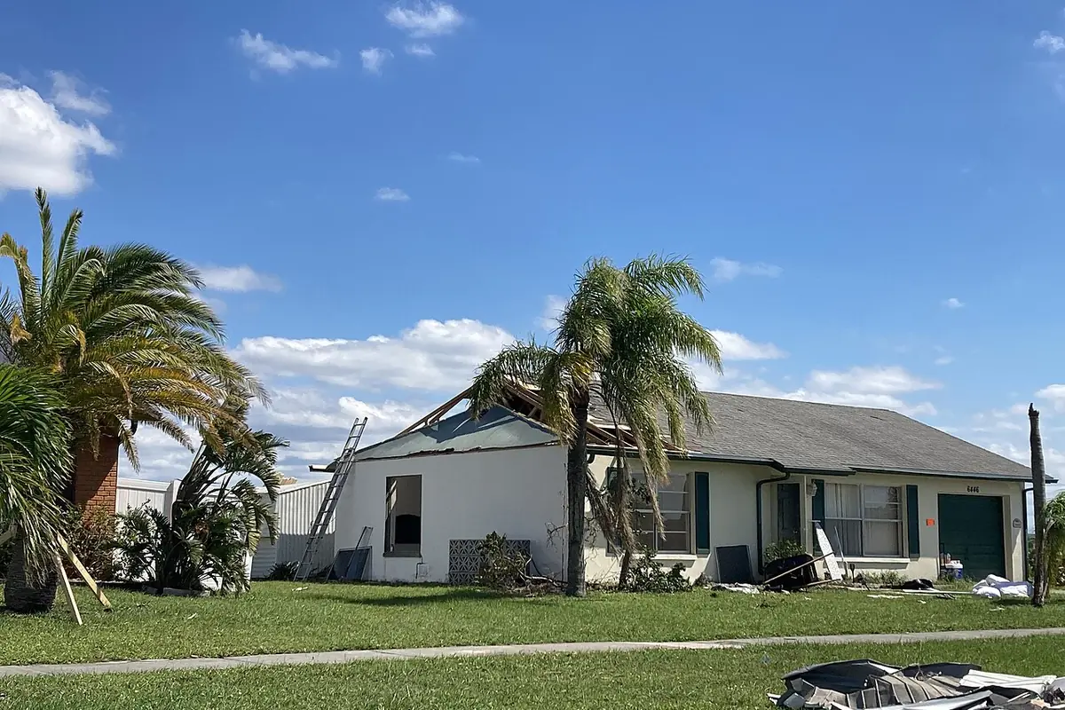 Single-story house with a torn-open roof and debris on the lawn after a hurricane