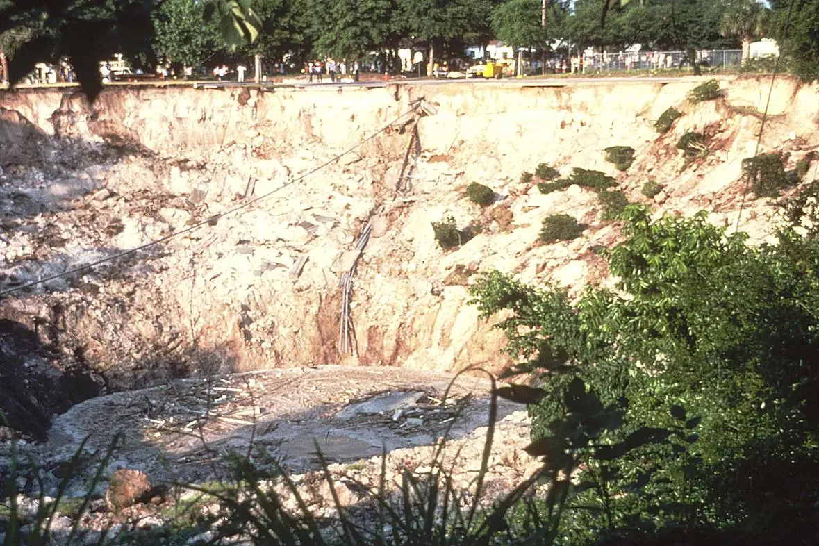 Large open sinkhole with steep sandy limestone walls and debris at the bottom