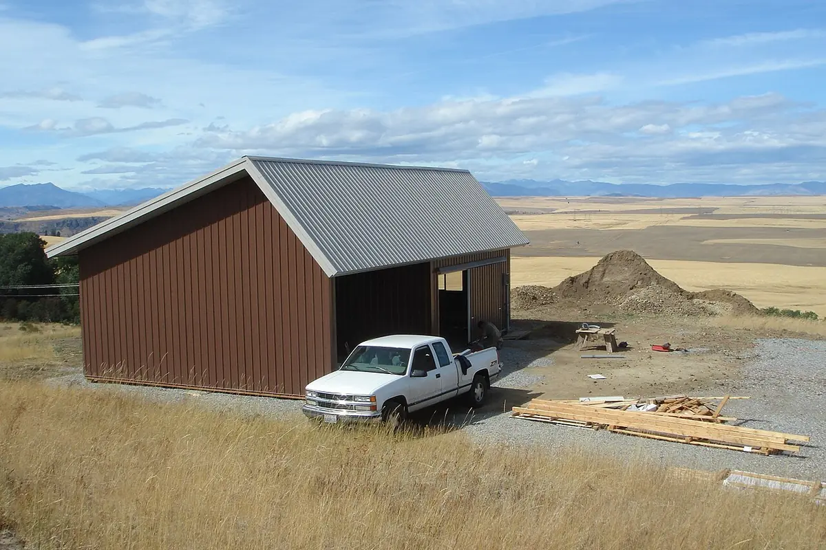 Brown metal pole barn with a white pickup parked at the open bay