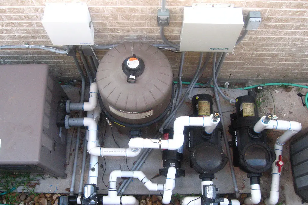 Pool filter, two pumps and PVC plumbing on a concrete pad against a house wall