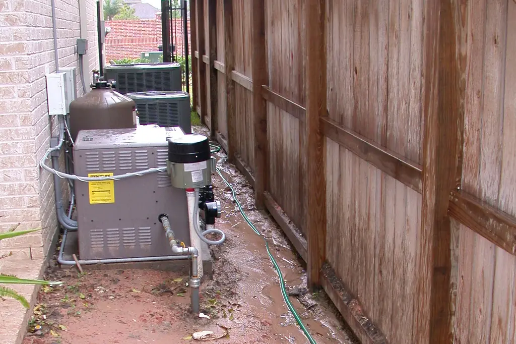Pool heater and filter on a pad in a narrow side yard beside AC condensers