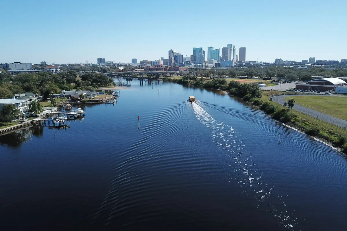 Aerial view of a river with a water taxi wake leading to a downtown skyline