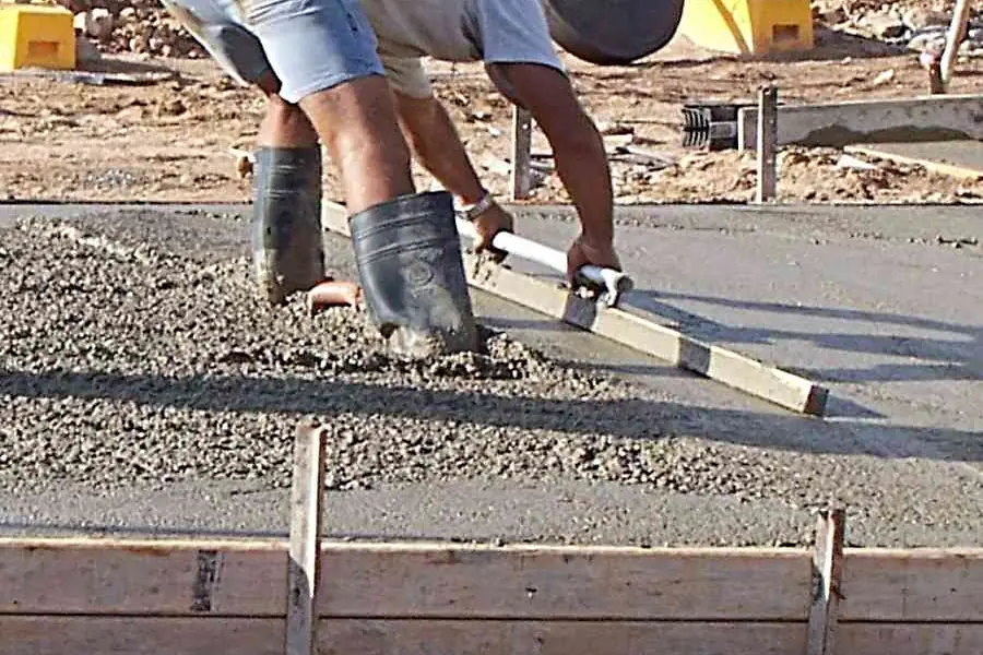 Worker pulling a screed board across wet concrete between wood forms