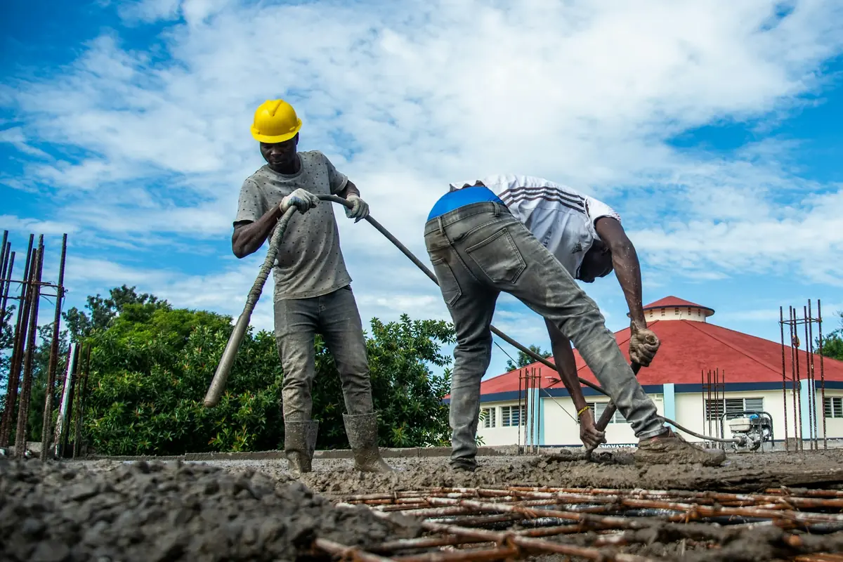 Two workers spreading concrete over a rebar mat on a sunny day