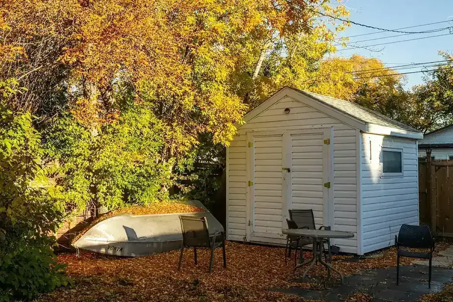 White vinyl shed beside a small paved sitting area